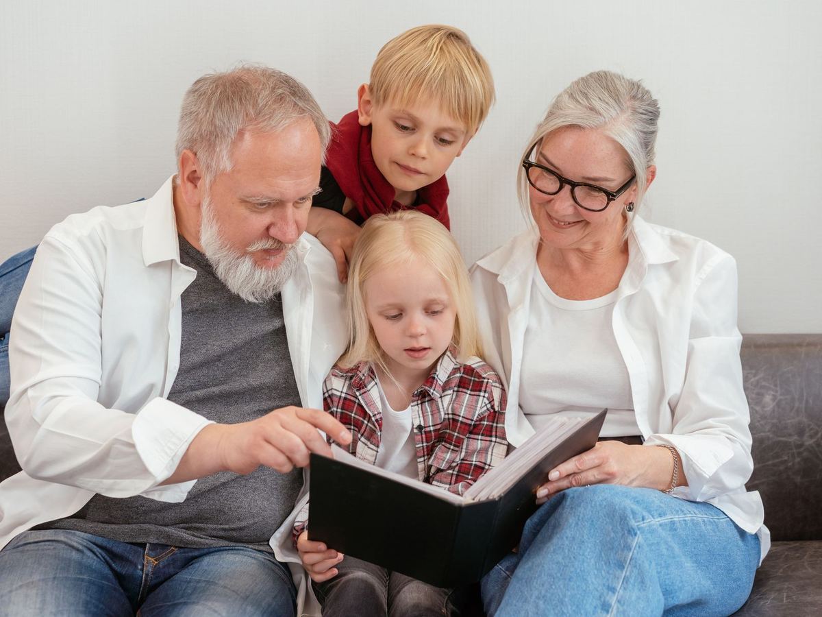 Grandparents reading a book with their two grandchildren on the sofa