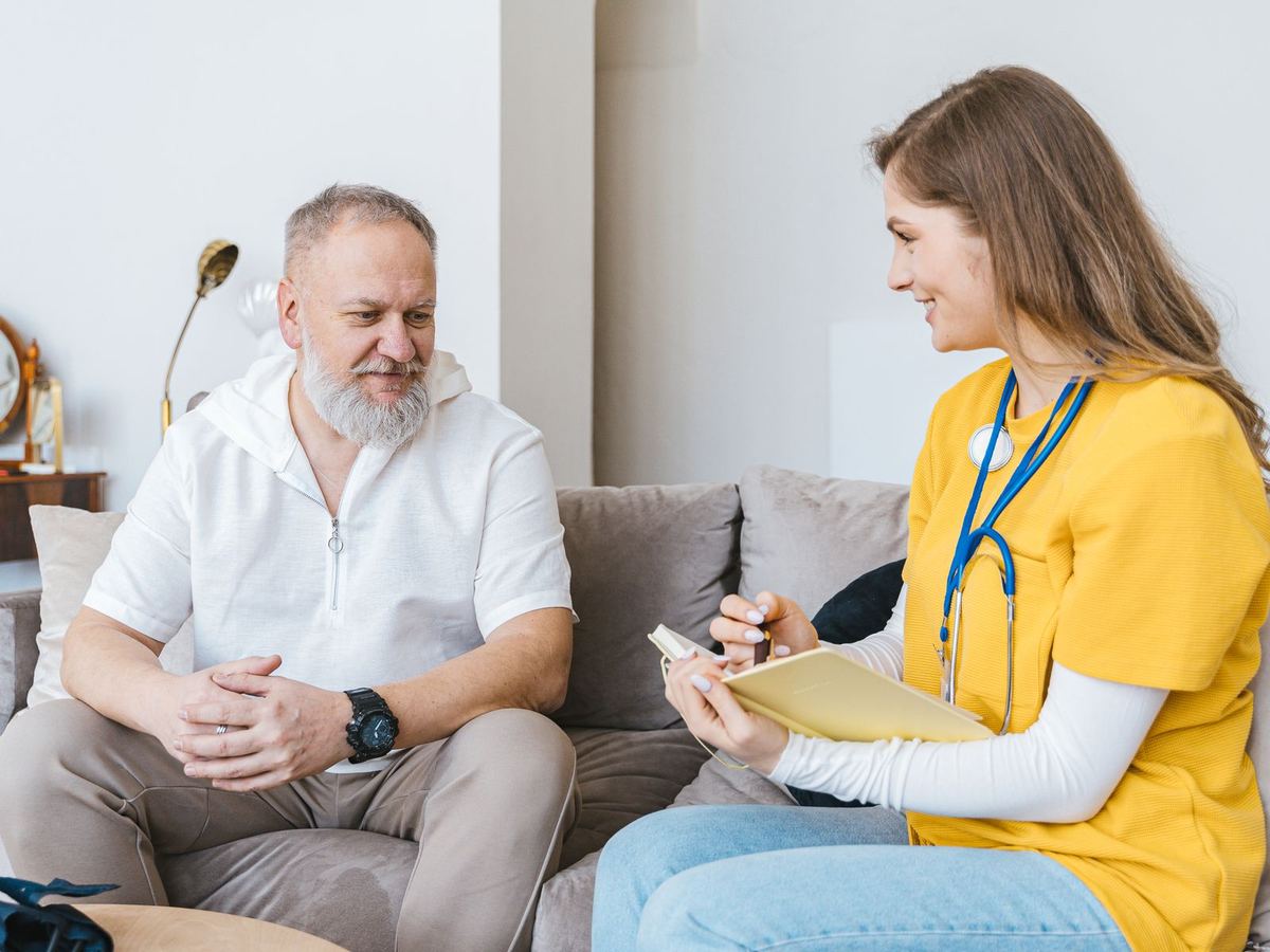 Home health nurse talking with a smiling older man in his living room